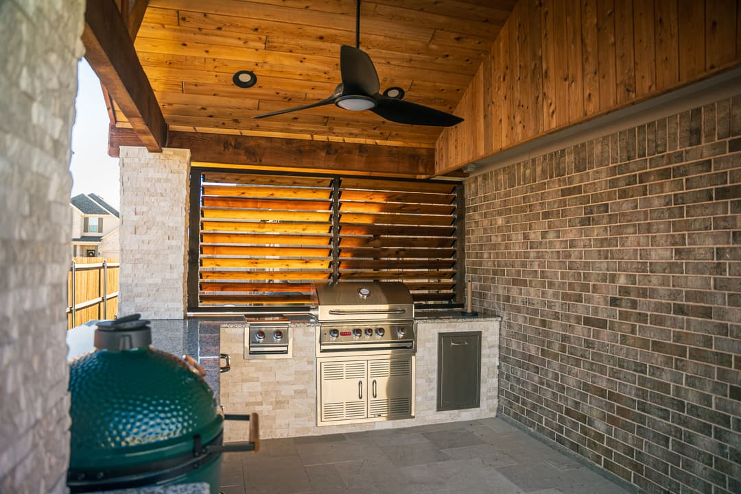 Outdoor kitchen featuring a stainless steel grill, stone backsplash, and wooden ceiling.