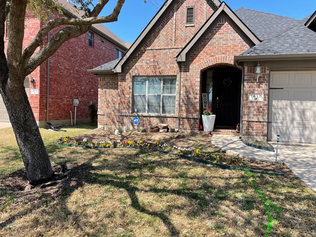 Brick house exterior with garden, landscaping, and driveway on sunny day.