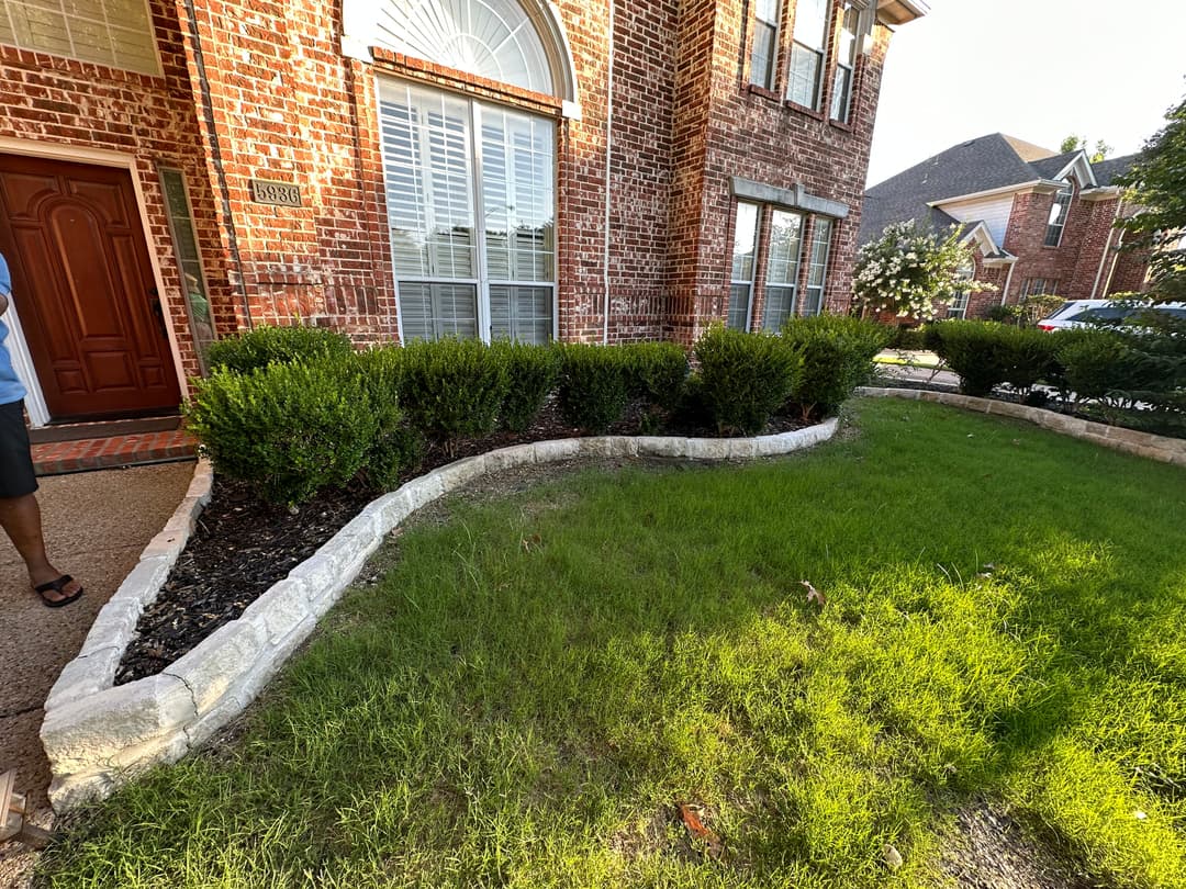 Front yard landscaping featuring a curved stone border, green grass, and well-trimmed bushes.