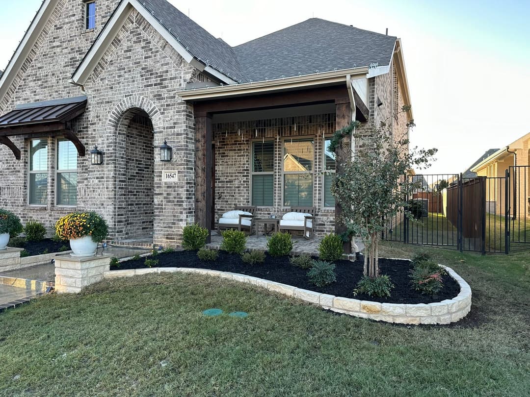 Brick house exterior with landscaped front yard, porch seating, and flower pots.