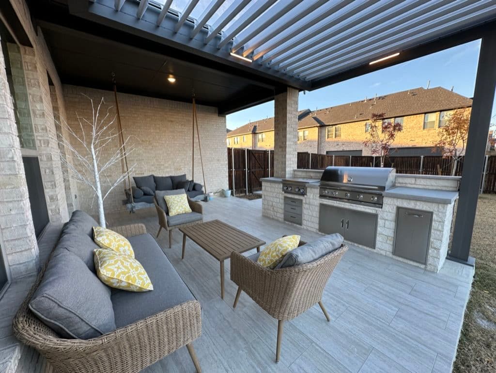 Modern outdoor patio with seating, table, and stainless steel grill under a covered roof.