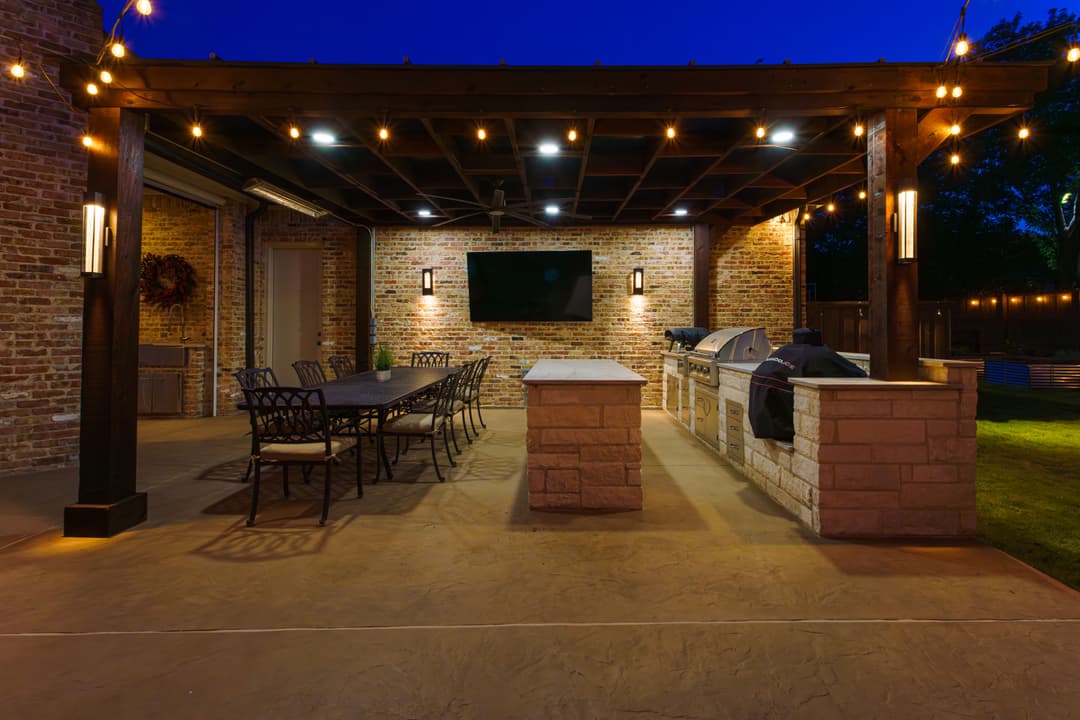Elegant outdoor kitchen with cozy lighting, grilling station, and dining area at dusk.