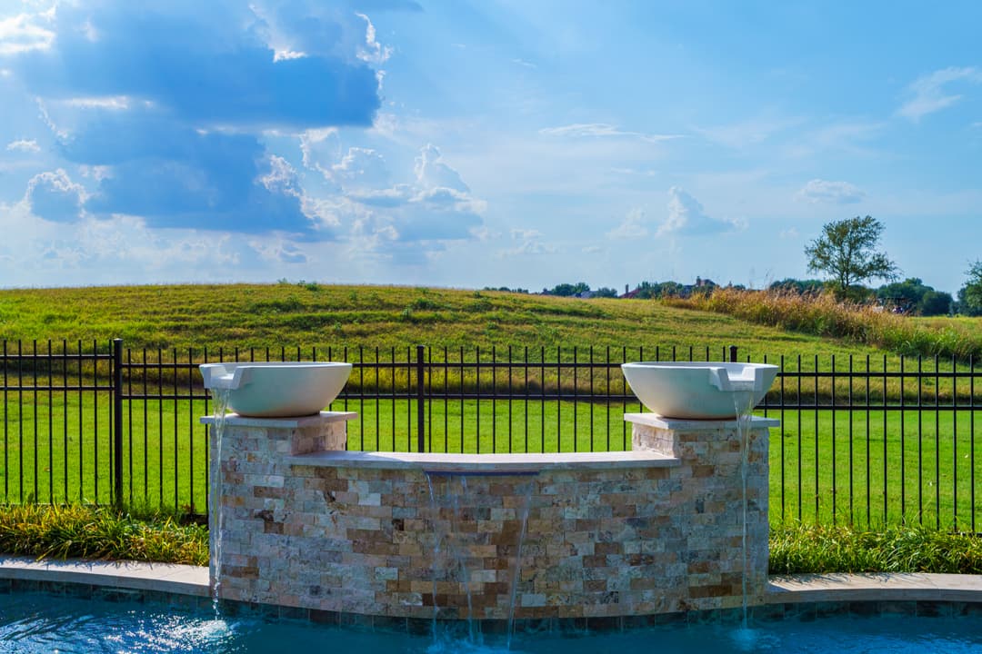 Elegant outdoor fountain with two basins against a scenic green landscape and blue sky.