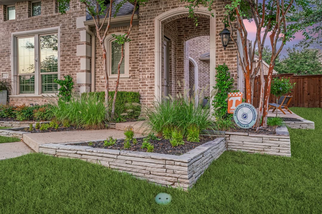 Beautiful landscaped home entrance with stone features, lush greenery, and decorative signage.
