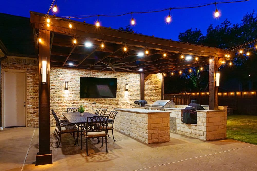 Elegant outdoor patio with string lights, grilling station, and dining area at night.