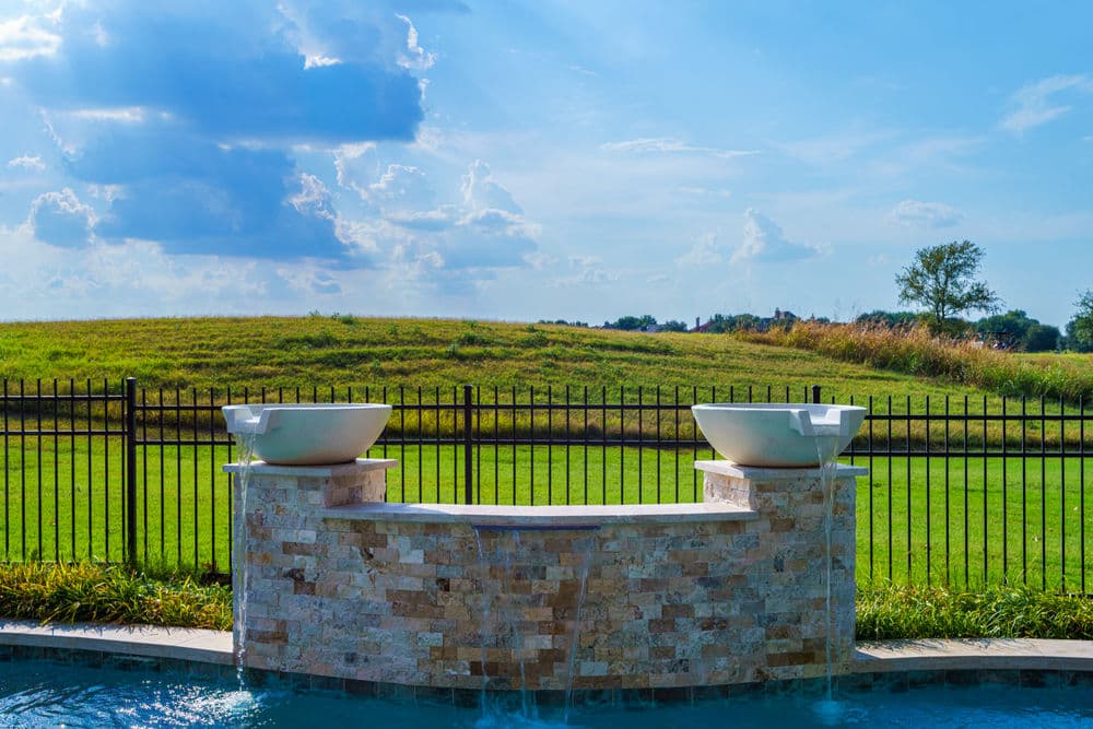 Modern outdoor fountain with two bowls overlooking a green landscape under a blue sky.
