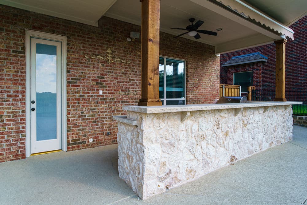 Outdoor patio area with stone bar, wooden supports, and access door near red brick wall.